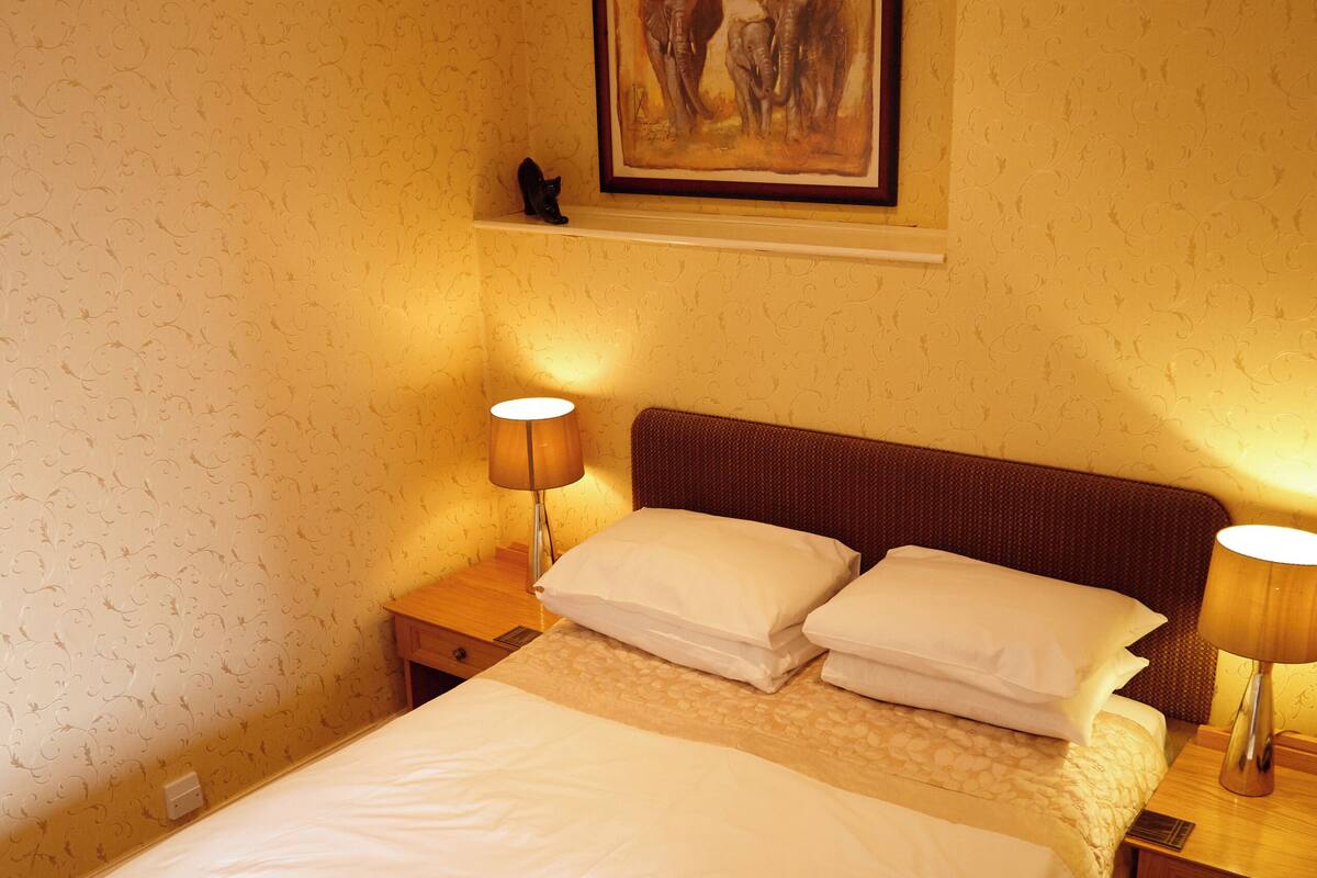 A hotel room with a large bed, two bedside tables, a nightstand, a framed artwork above the bed, and a carpeted floor.