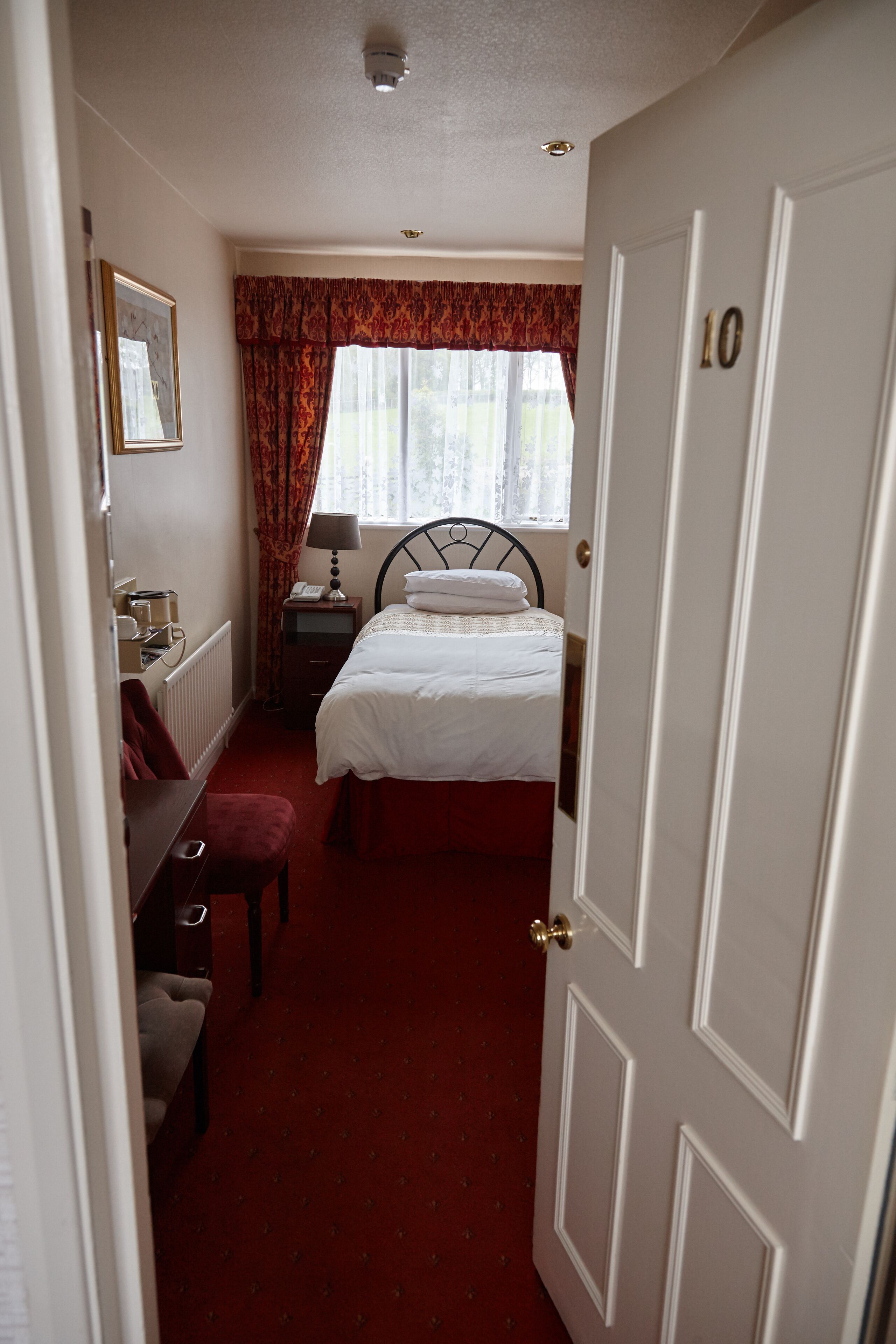 A hotel room with a bed, a nightstand, a lamp, a dresser, and a window with curtains.