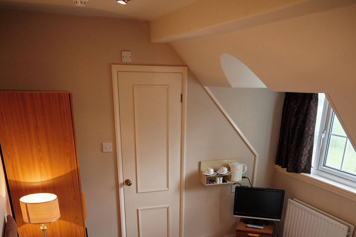 A hotel room with a large bed, a bedside table with a lamp, a TV, and a window with curtains.