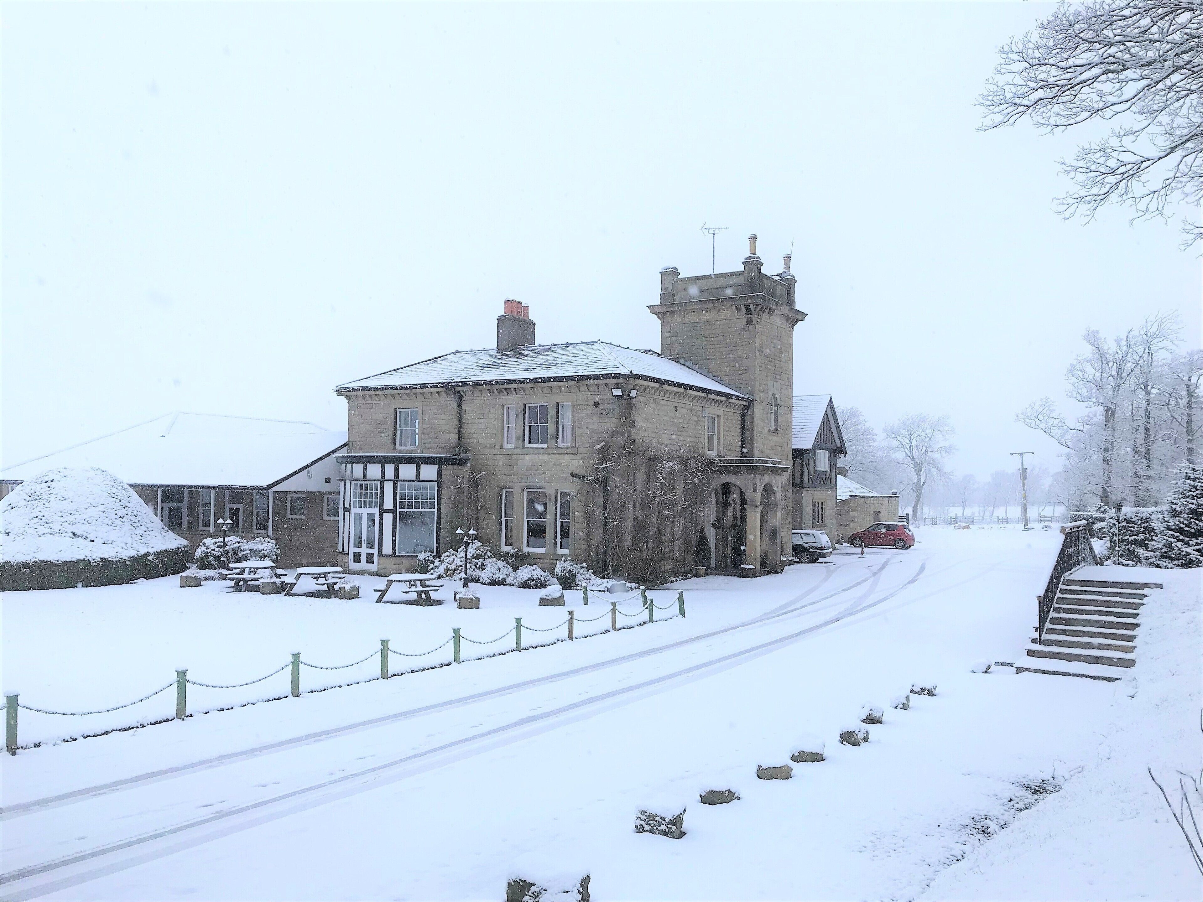 A stone building with a tower, a snow-covered road, and a picnic area.