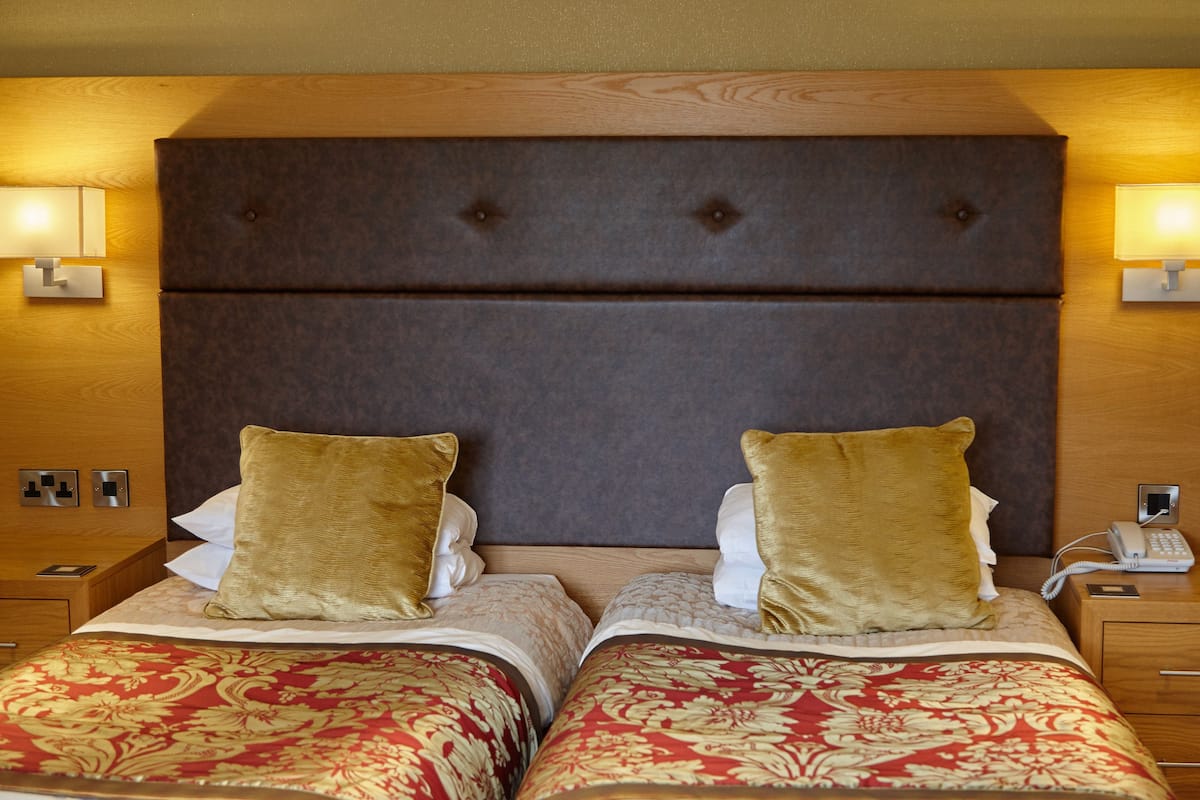 A hotel room with two beds, each with a headboard, bedside lamps, and a telephone on the nightstand.