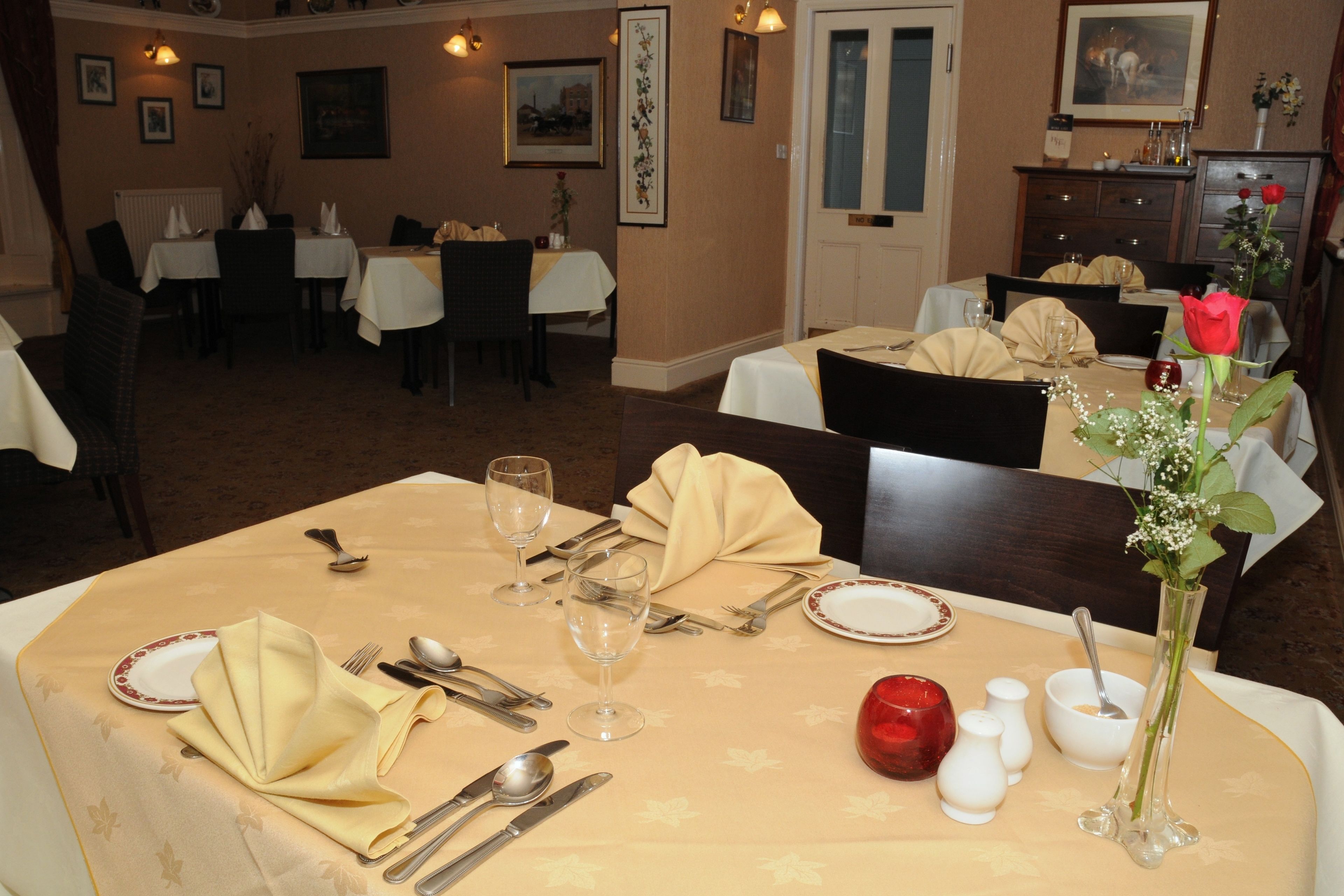 Un espace repas avec des tables mises pour le repas, comprenant des couverts, des assiettes et des verres.