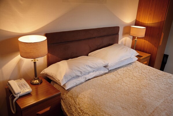 A hotel room with a bed, two bedside lamps, a telephone, and a wooden nightstand.