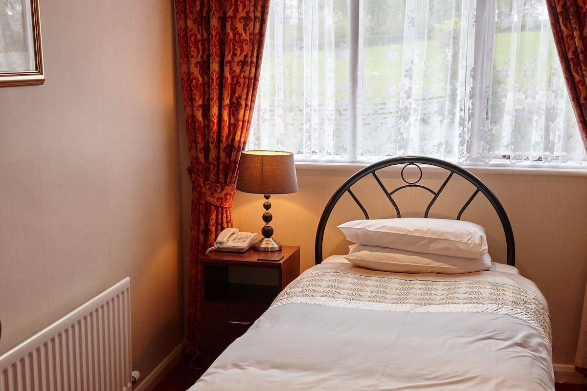 A neatly made bed with white linens, a bedside lamp, and a telephone on a nightstand.