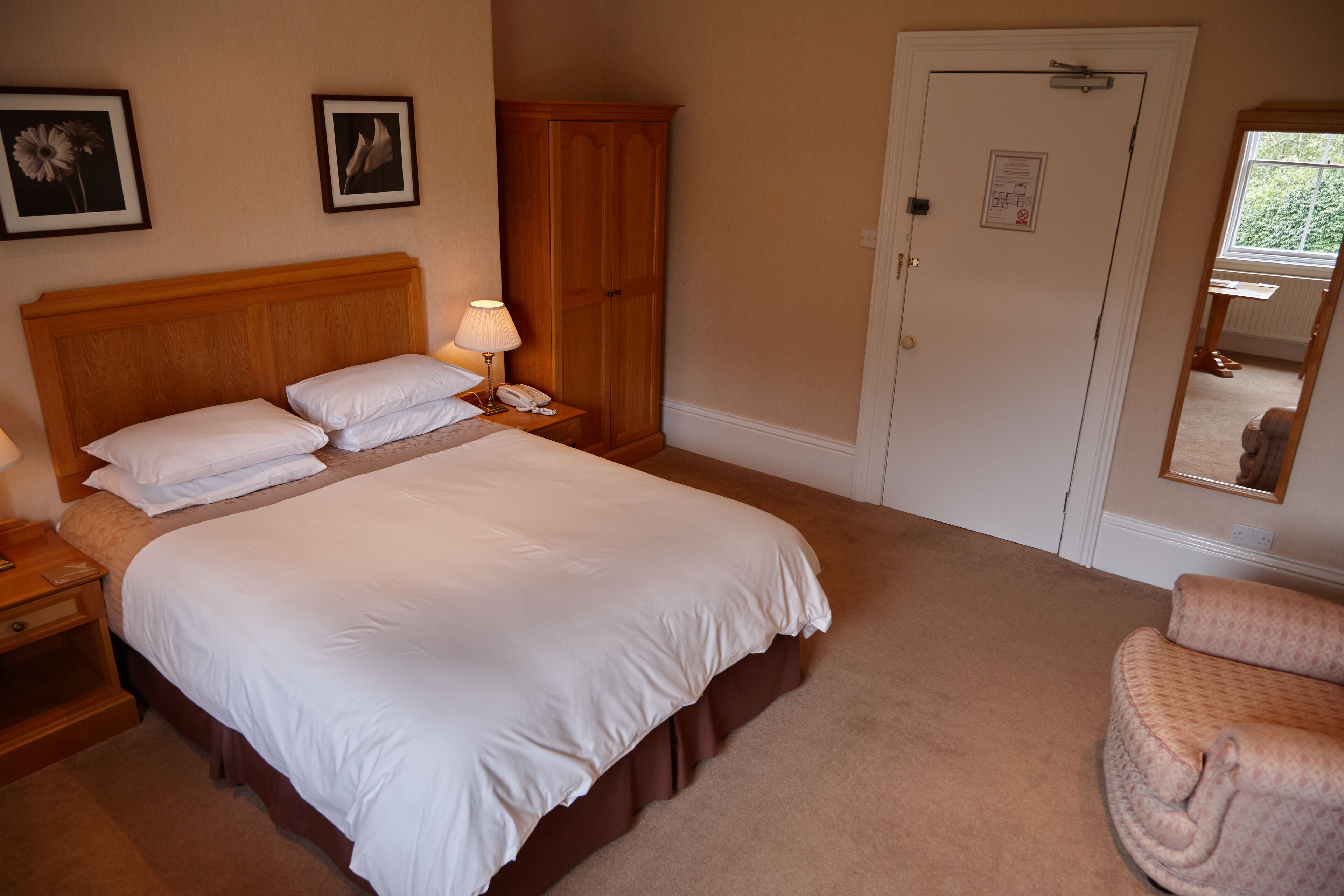 Een slaapkamer met een groot bed, een nachtkastje, een houten kledingkast, een deur met een bericht en een spiegel.