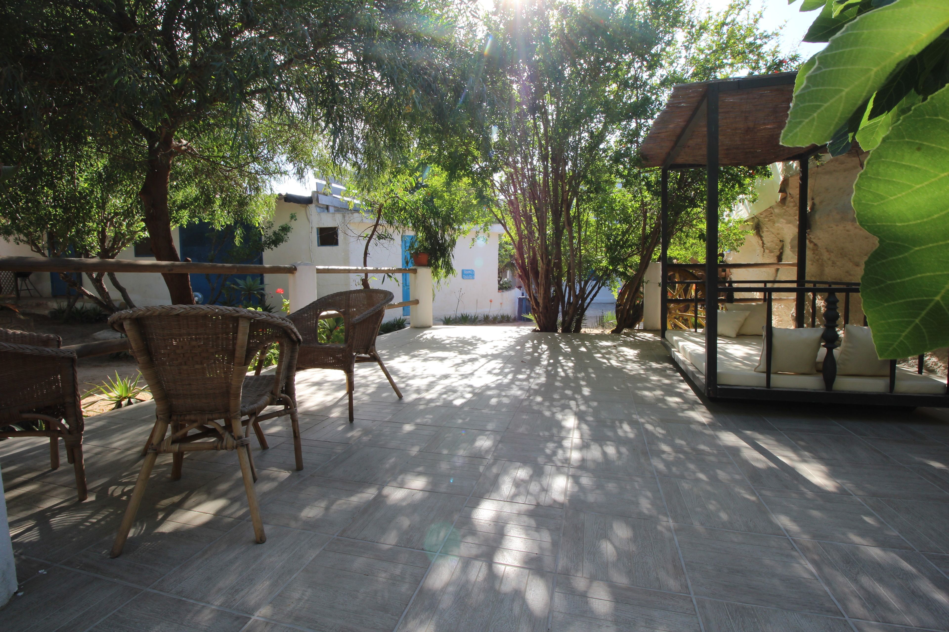 An outdoor patio area with wicker furniture, a covered seating area, and a view of buildings in the background.
