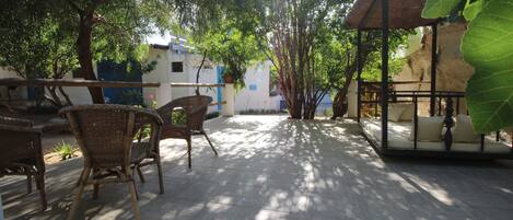 An outdoor patio area with wicker furniture, a covered seating area, and a view of buildings in the background.