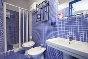 A bathroom with blue-tiled walls, a white sink, and two toilets. - L'Oasi Villaggio Albergo (Favignana)