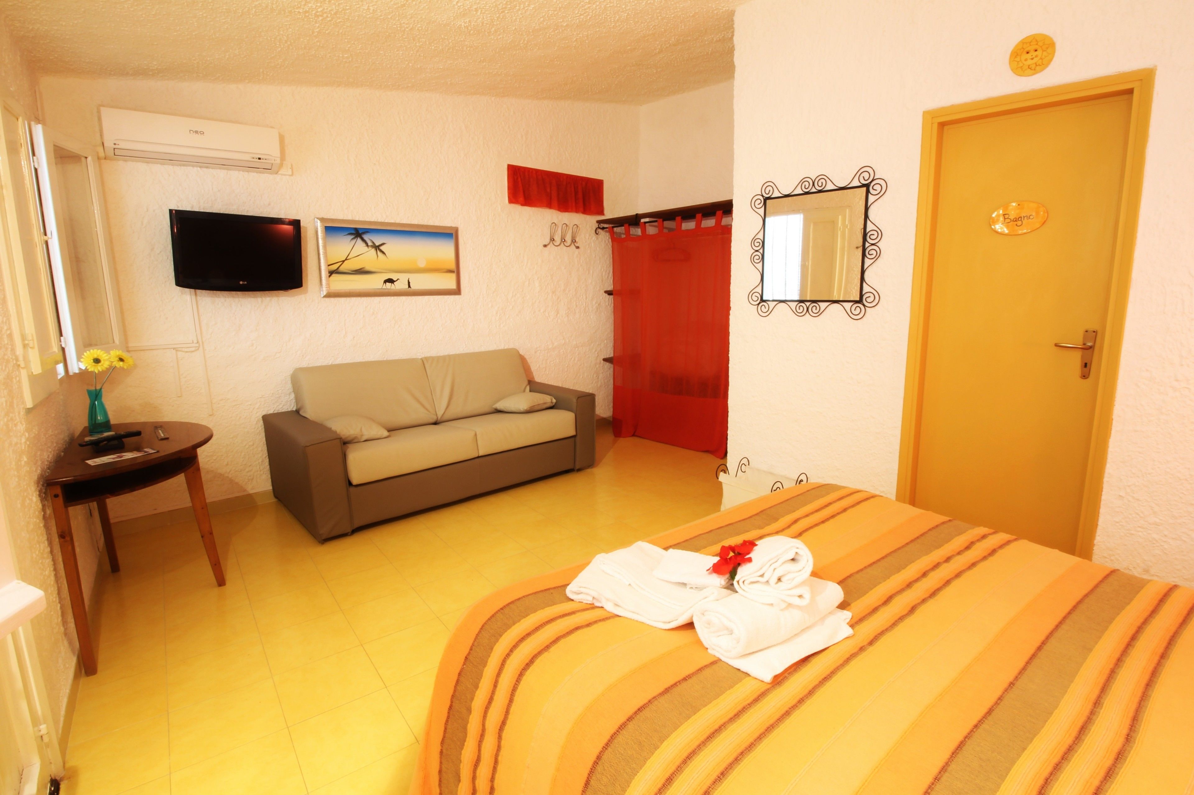 A hotel room with a bed, a sofa, a TV, a mirror, and a door.