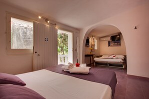 A hotel room with a large bed, a smaller bed, a TV, and a balcony with a view of greenery. - L'Oasi Villaggio Albergo (Favignana)