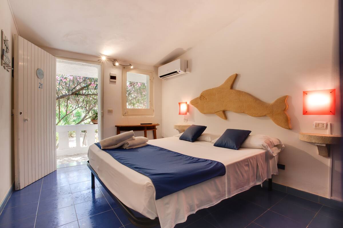 A bedroom with a bed, a wall-mounted fish sculpture, a window, and an air conditioning unit.