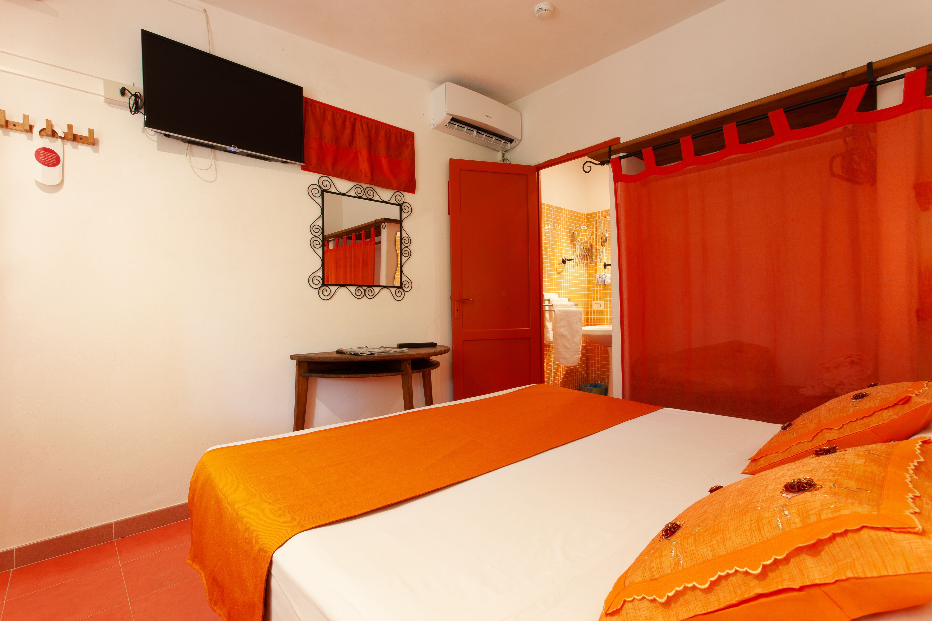 Un dormitorio con cama, televisor, espejo y aire acondicionado.