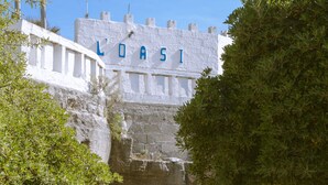 Un arco in pietra conduce a un edificio con la scritta 'LOASI', immerso nel verde sotto un cielo sereno.