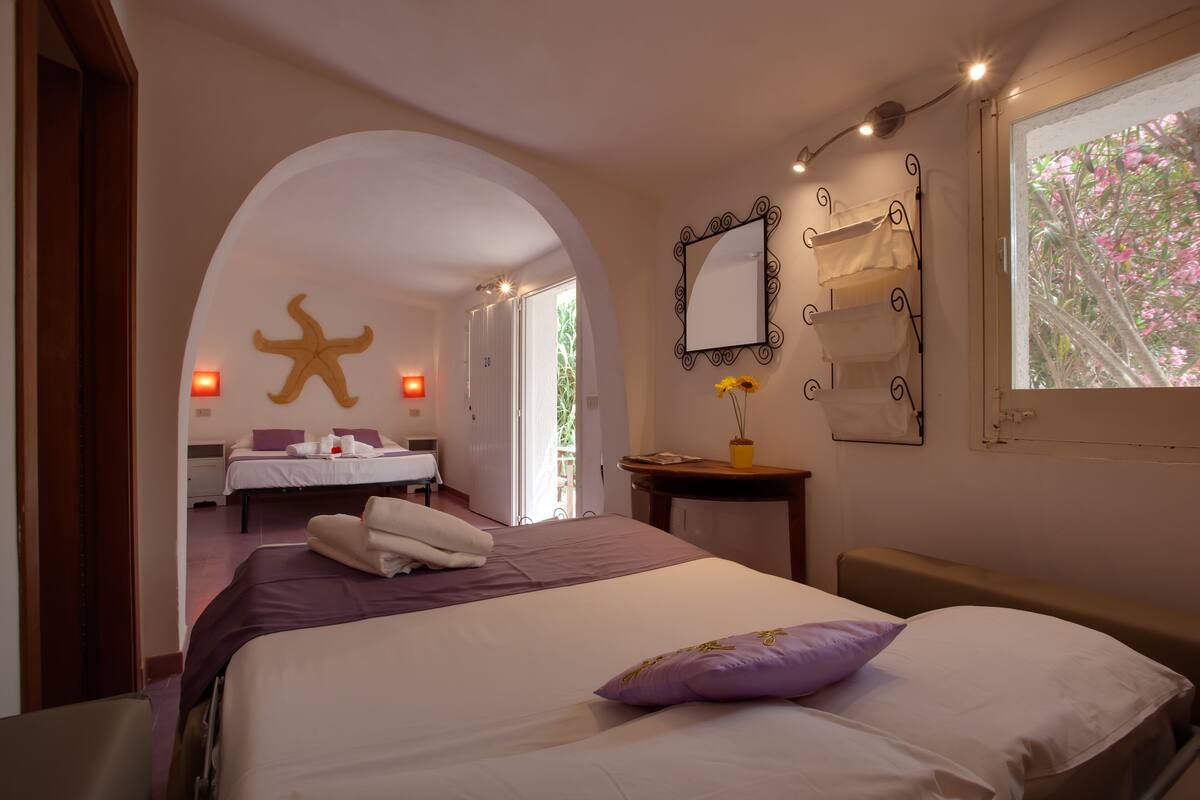 A hotel room with a large bed, a vanity with a mirror, and a view of a garden.