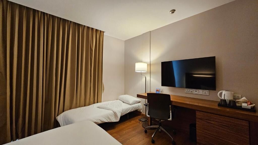 A hotel room with a bed, a desk, a chair, a television, and a lamp.