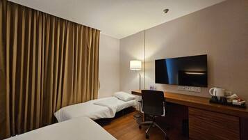 A hotel room with a bed, a desk, a chair, a television, and a lamp.