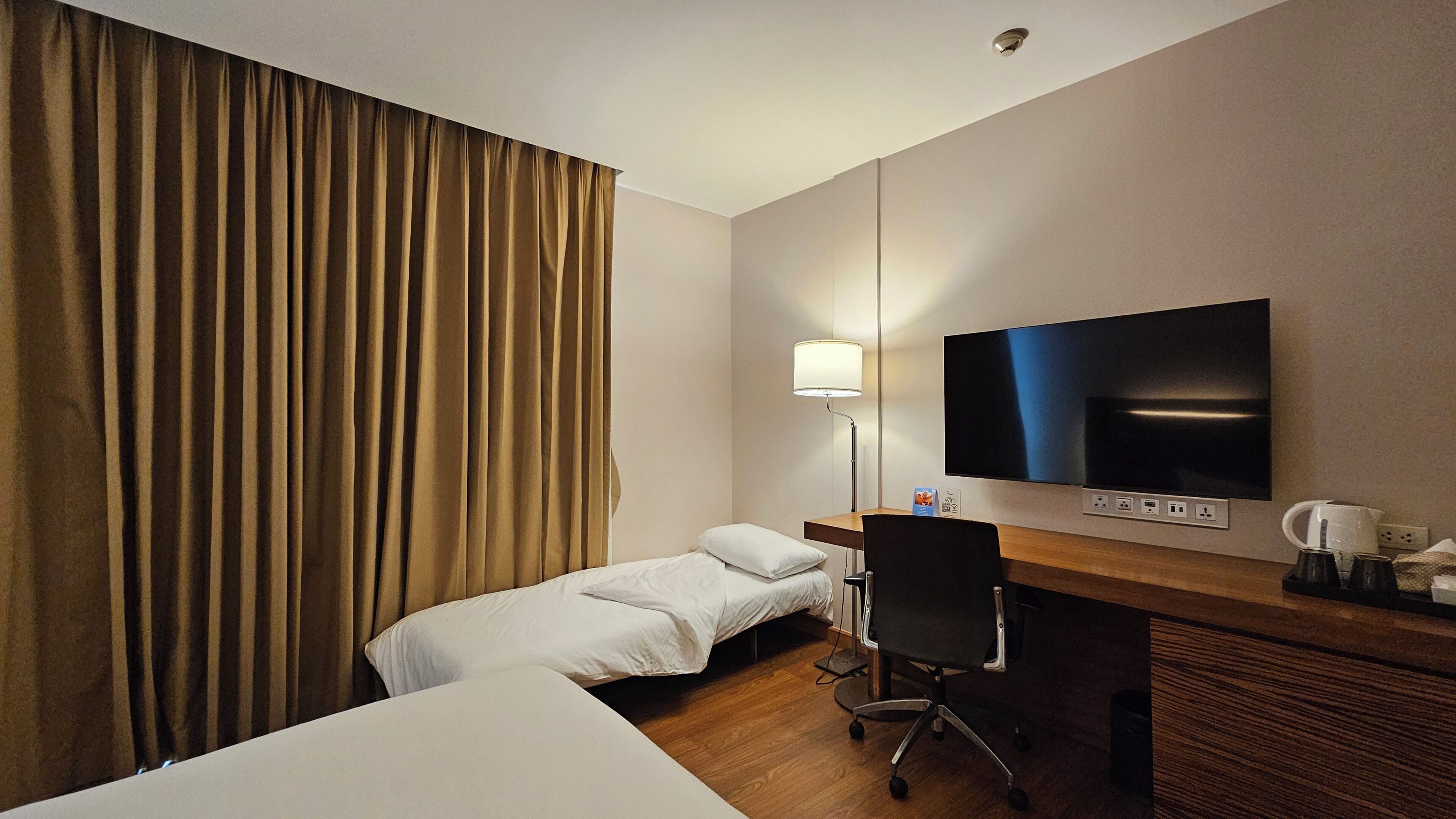 Une chambre d’hôtel avec un lit, un bureau, une chaise, une télévision et une lampe.