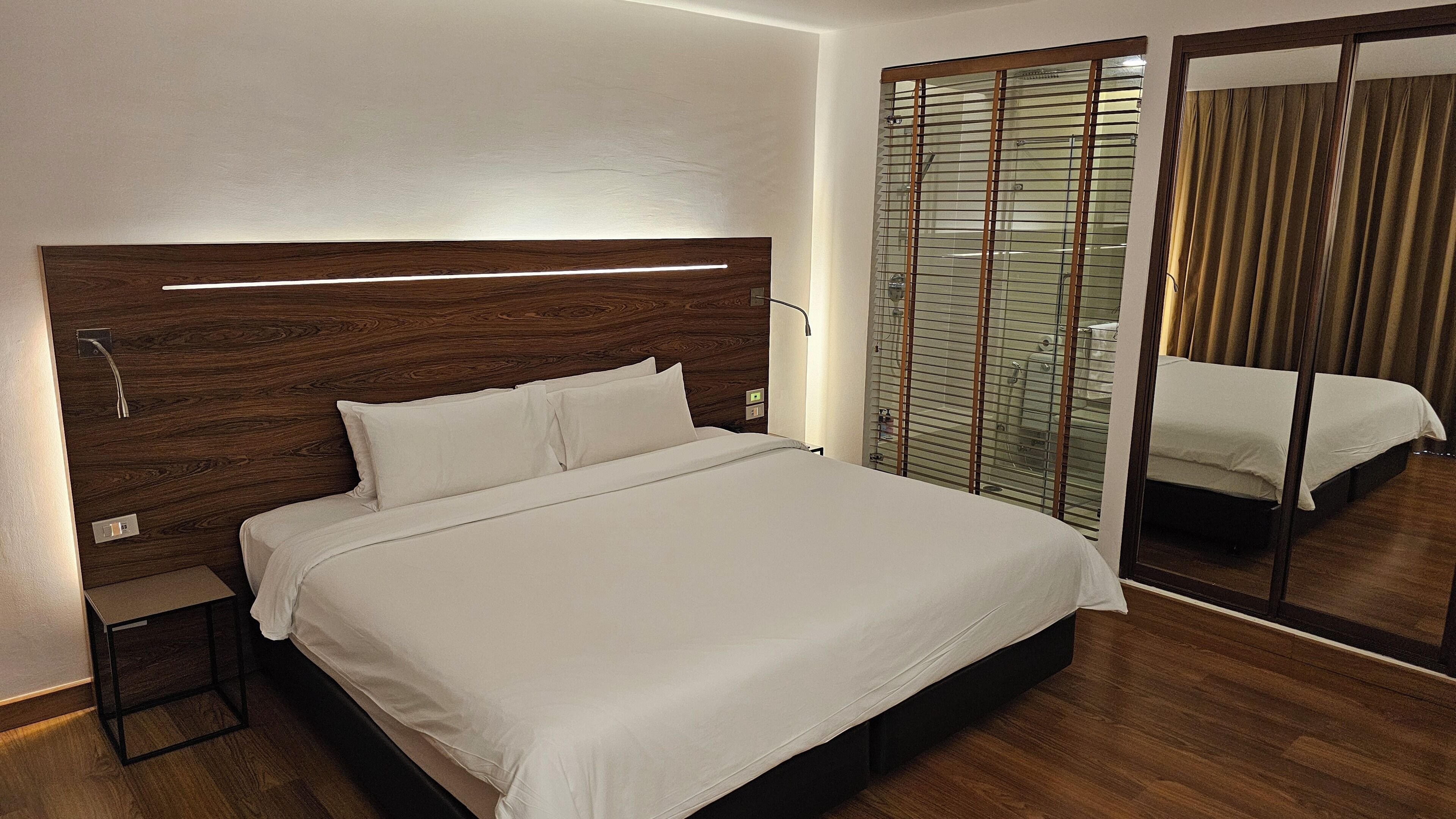 Ein modernes Hotelzimmer mit einem hölzernen Kopfteil, einem großen Bett, einem Nachttisch und einem Spiegel.