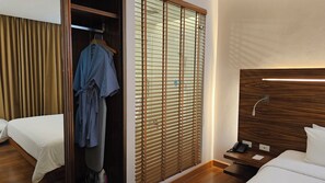 A hotel room with a wooden wardrobe, a bed, a bedside table with a phone, and a window with blinds. - Sachas Hotel Uno Asoke Sukhumvit Bangkok (Bangkok)