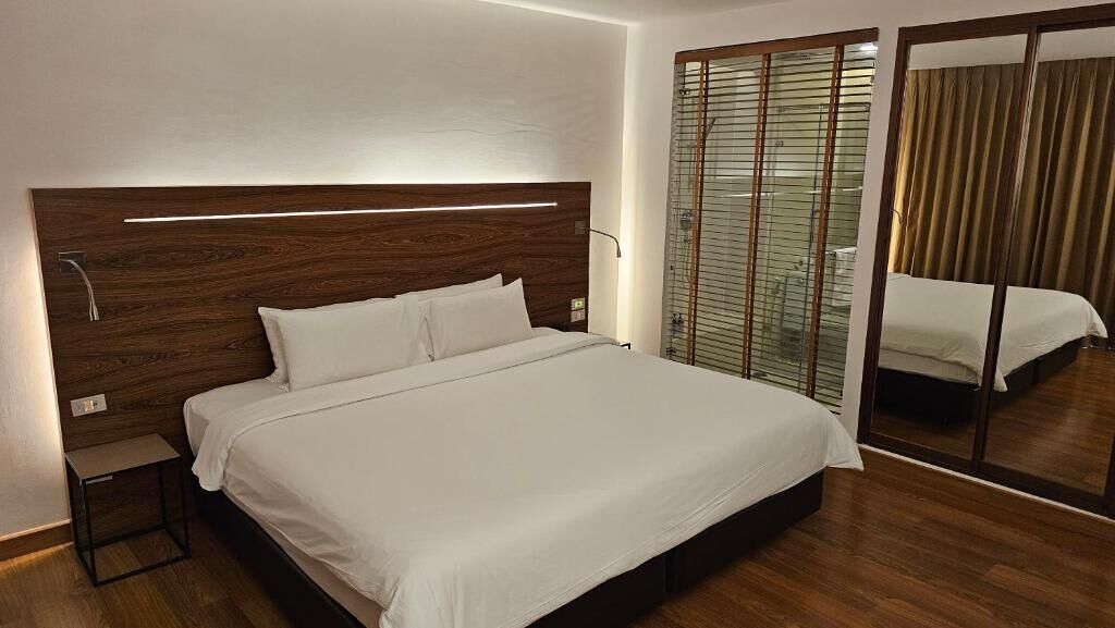 Un dormitorio moderno con cabecera de madera, cama grande, mesita de noche y separador de vidrio con puerta corrediza.