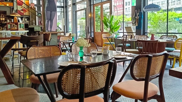 An indoor dining area with large windows, wicker chairs, and a variety of table settings. - Sachas Hotel Uno Asoke Sukhumvit Bangkok (Bangkok)
