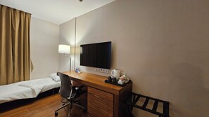 Habitació d'hotel amb un llit individual, escriptori amb cadira, televisió de pantalla plana, làmpada i cafetera.