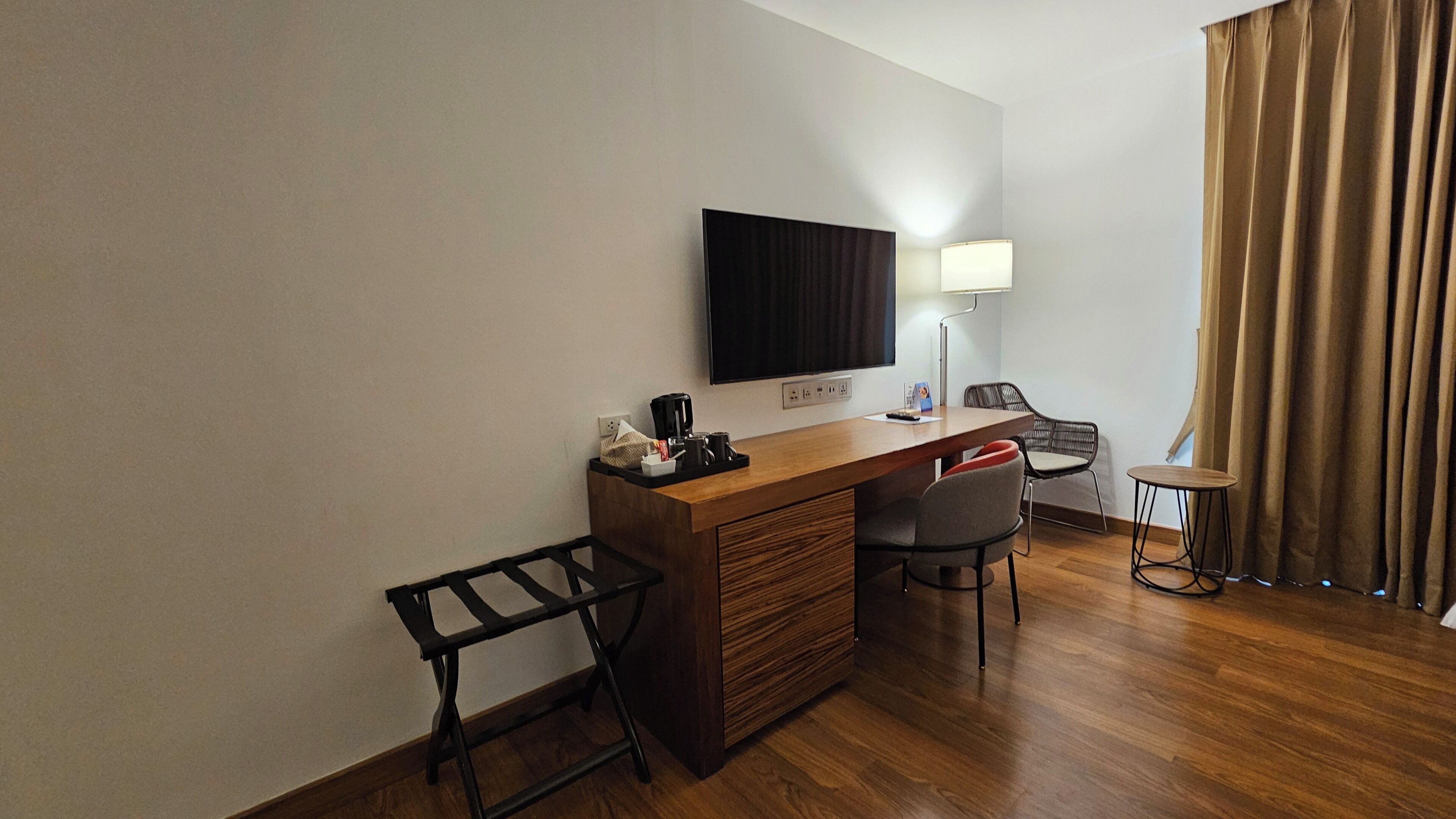 Una habitación de hotel con un escritorio de madera, una televisión, una lámpara, una silla y una mesita.