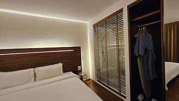 A hotel room with a bed, a nightstand, a robe hanging on a door, and a window with blinds.