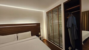 A hotel room with a bed, a nightstand, a robe hanging on a door, and a window with blinds. - Sachas Hotel Uno Asoke Sukhumvit Bangkok (Bangkok)