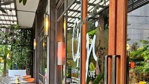 An outdoor cafe with tables and chairs, a wooden facade, and a glass window with a cafe sign. - Sachas Hotel Uno Asoke Sukhumvit Bangkok (Bangkok)