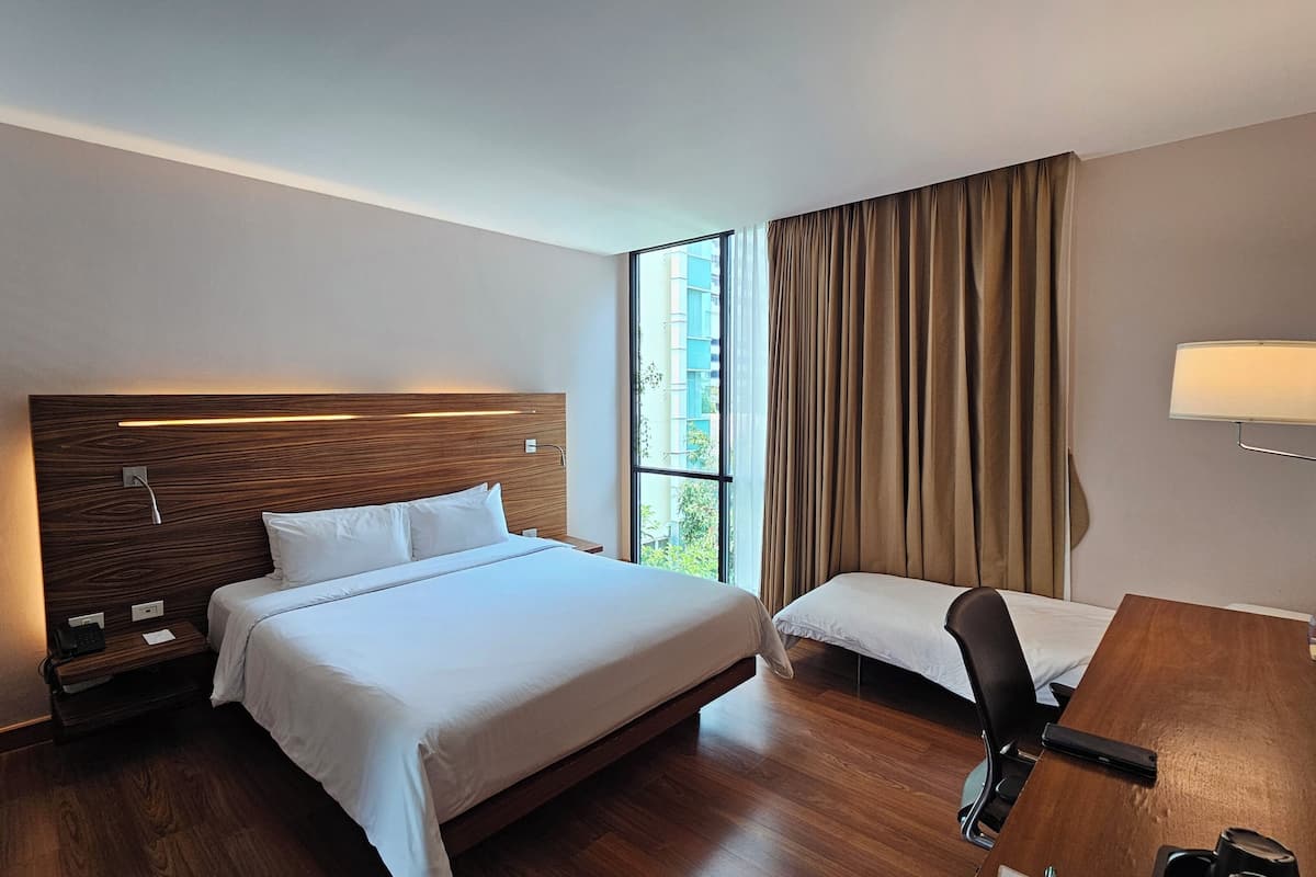 A hotel room with a large bed, a desk, a chair, a lamp, and a window with curtains.