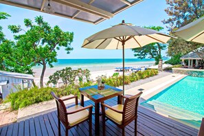 Una terraza con mesa y sillas, con vista a una playa y una piscina.