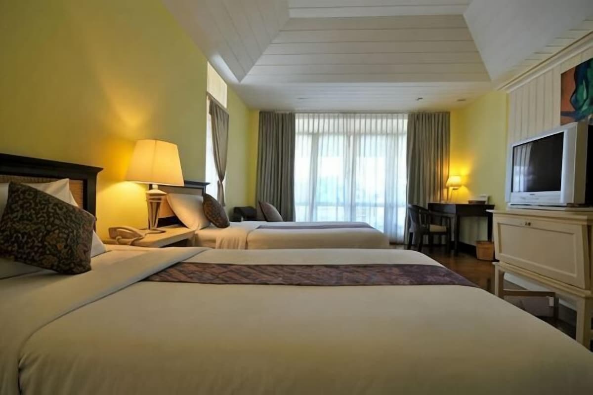 Quarto de hotel com duas camas, uma mesa de trabalho com cadeira, televisão e janela com cortinas.