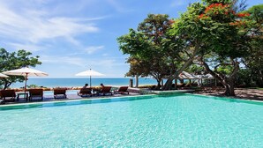 A pool area with lounge chairs and umbrellas, overlooking a body of water. - Baan Bayan Beach Hotel (Hua Hin)