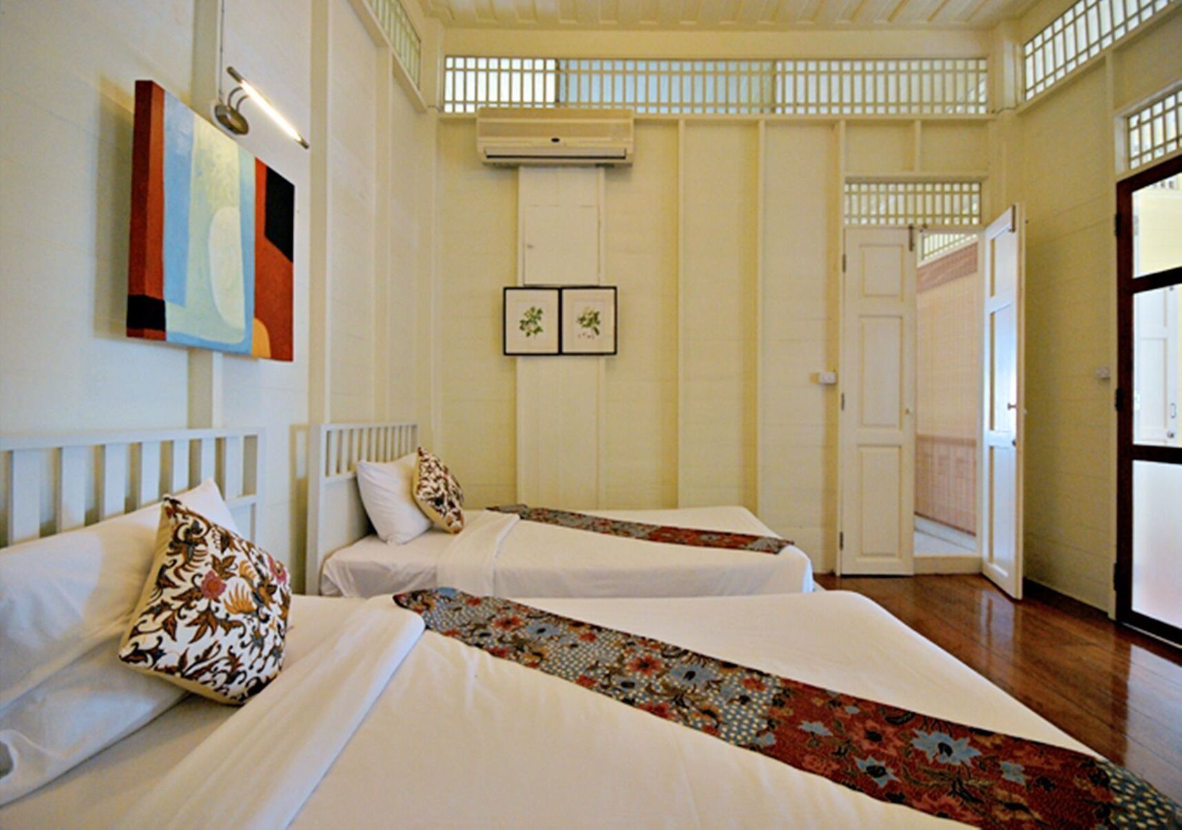 A hotel room with two beds, a window with bars, a door, and a wall-mounted air conditioner.