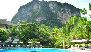 A pool area with lounge chairs and umbrellas, surrounded by lush greenery and a large cliff in the background. - Golden Beach Resort (Krabi)