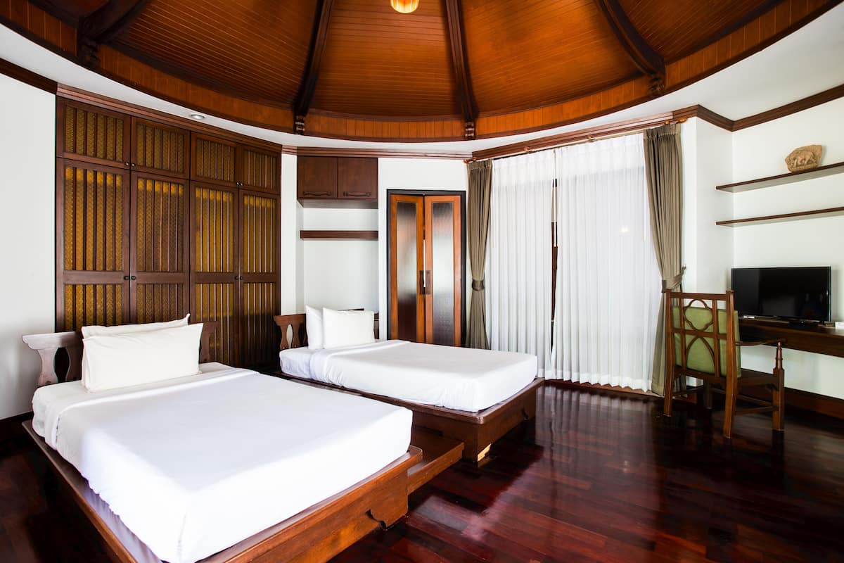 A hotel room with two beds, a wooden ceiling, a TV, and a desk.