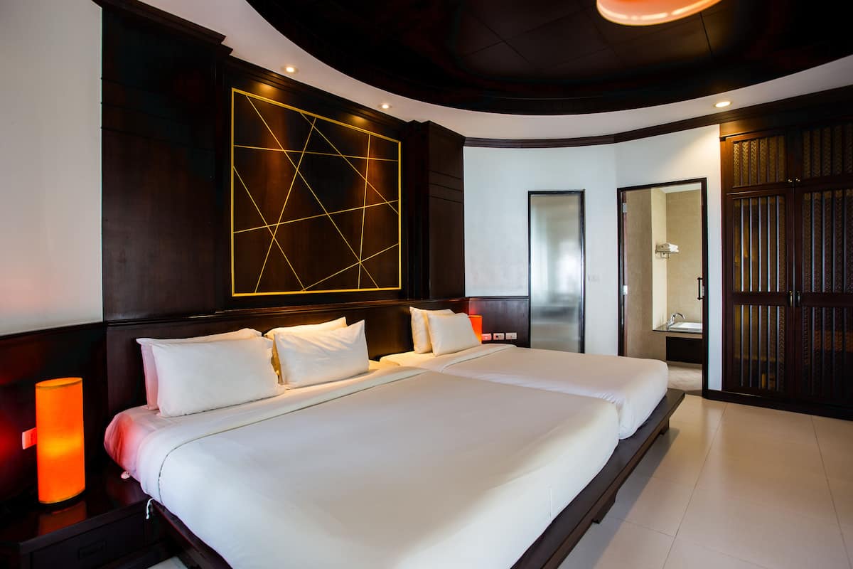 A modern hotel room with a large bed, a bedside table with a lamp, and a wall-mounted geometric light fixture.