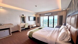 A hotel room with a bed, desk, chair, and a large window offering a city view. - Pailyn Hotel Phitsanulok (Phitsanulok)