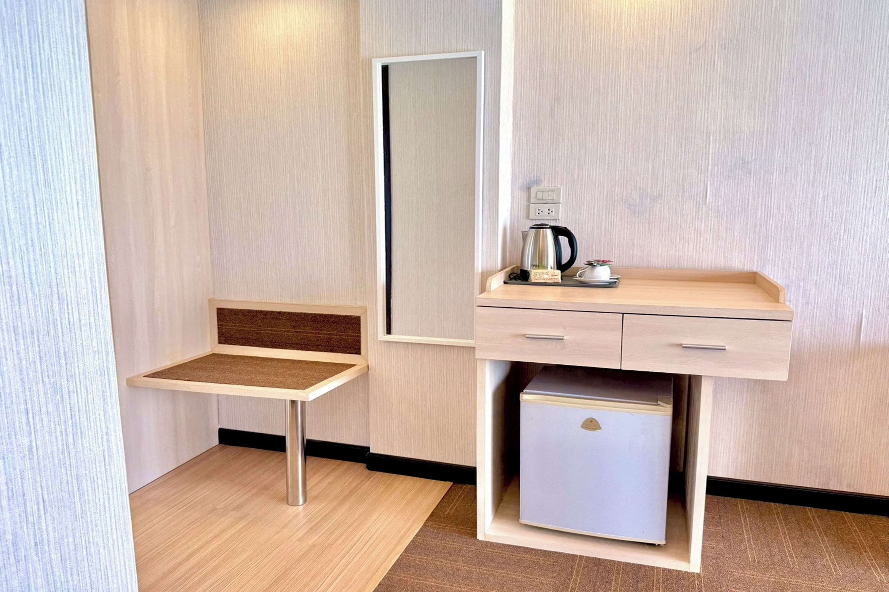 Kompakti hotellihuone, jossa on pieni työpöytä, peili, kahvinkeitin ja minijääkaappi.