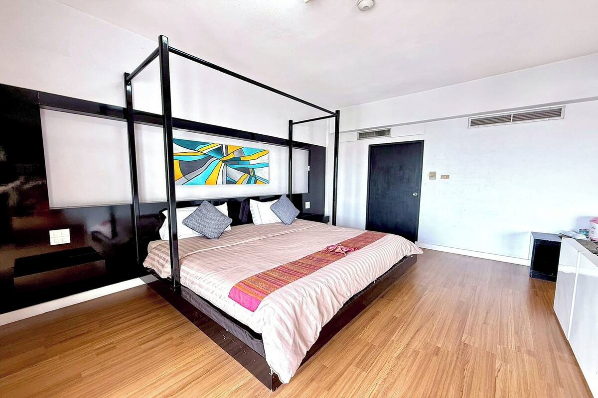 A modern bedroom with a four-poster bed, a large abstract painting, and a wooden floor.
