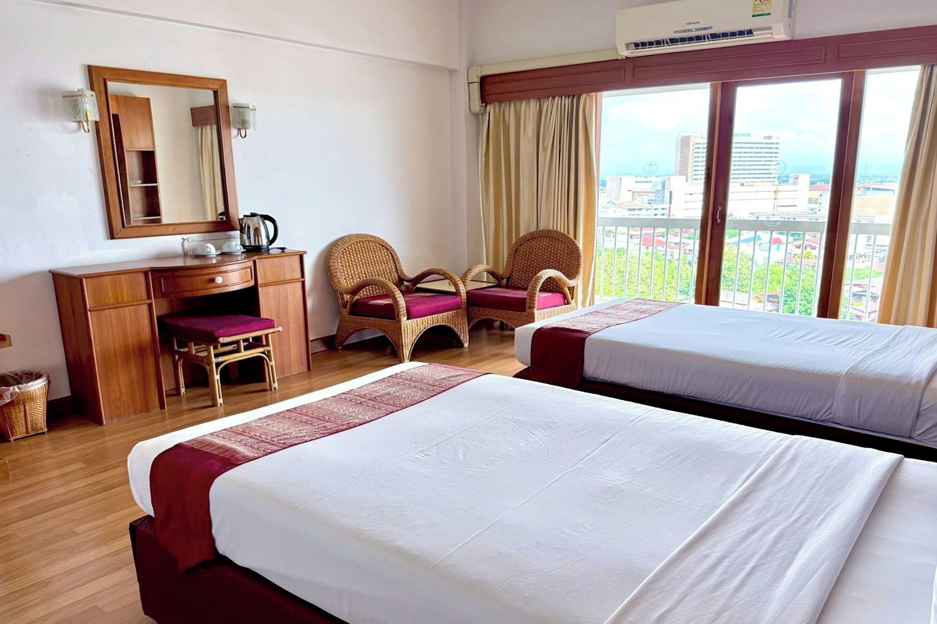 A hotel room with two beds, a wooden desk, a chair, a mirror, and a view of the city.