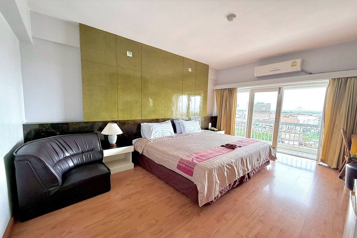 A hotel room with a bed, a sofa, a nightstand, and a large window with a city view.