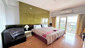 Habitación de hotel con cama, sofá, mesita de noche y un amplio ventanal con vista a la ciudad.