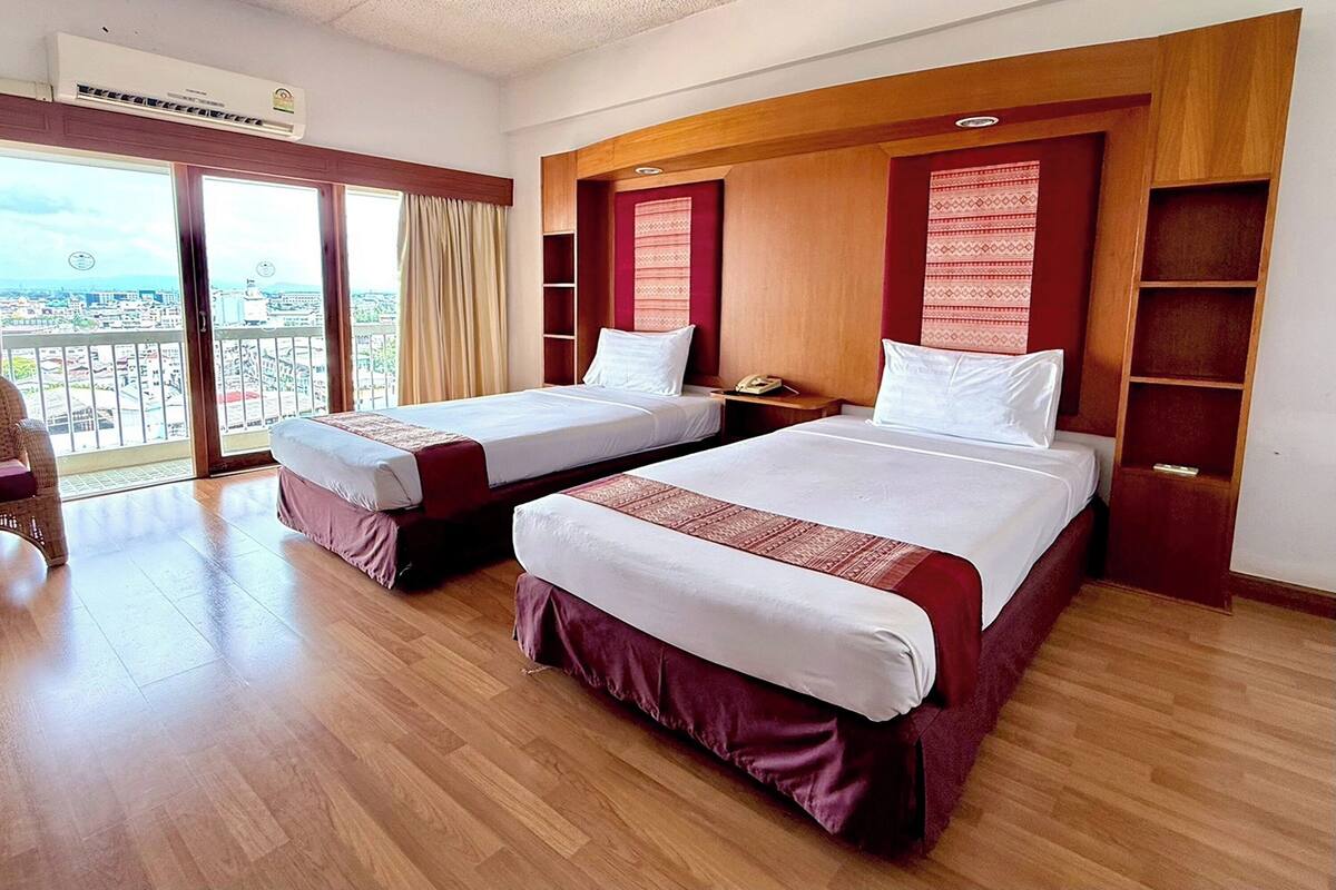 A hotel room with two beds, a balcony with a city view, wooden headboard, and a telephone on the nightstand.