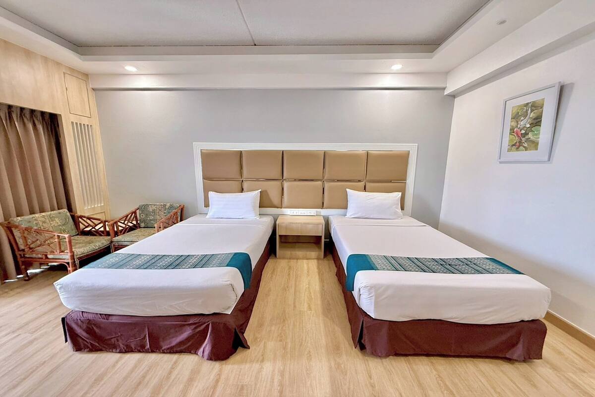 A hotel room with two single beds, a wooden headboard, a small table, and a sofa.