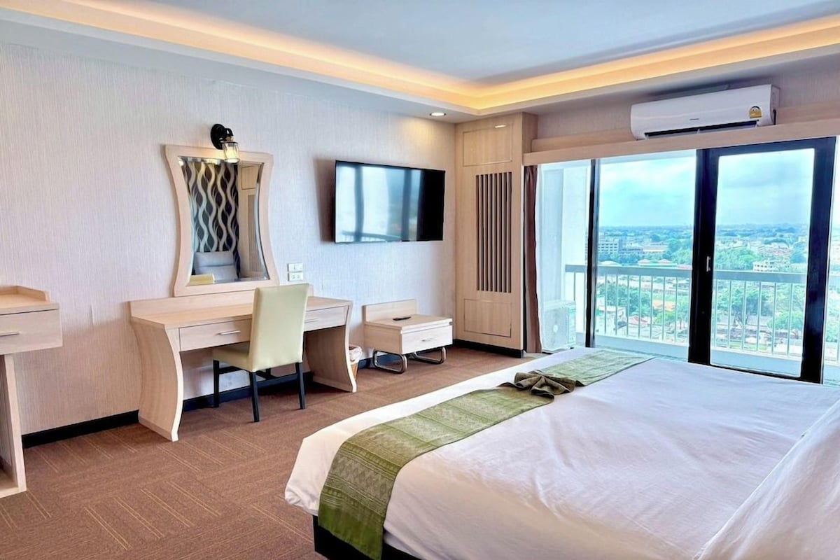 A hotel room with a bed, desk, chair, television, and a large window with a city view.