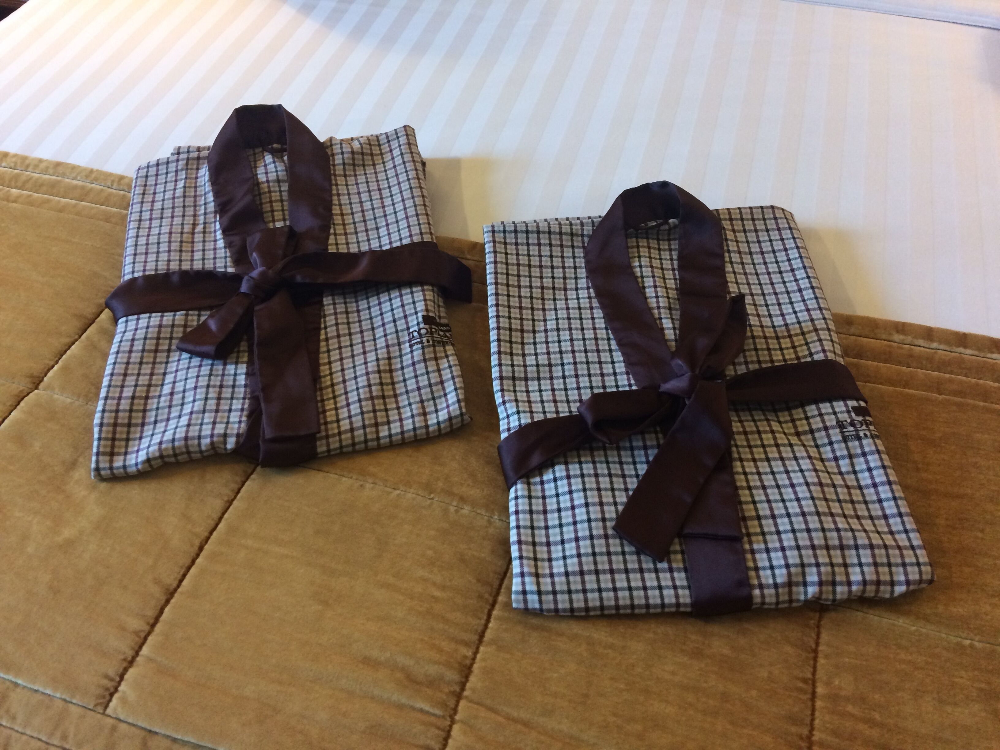 Two neatly wrapped gifts with brown ribbons on a bed with striped bedding.