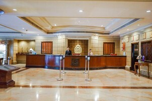 Zona de recepción de un hotel con piso de mármol, mostrador de recepción y una pared decorativa detrás del mostrador.