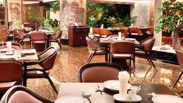 A restaurant with multiple tables and chairs, some with white tablecloths and napkins.